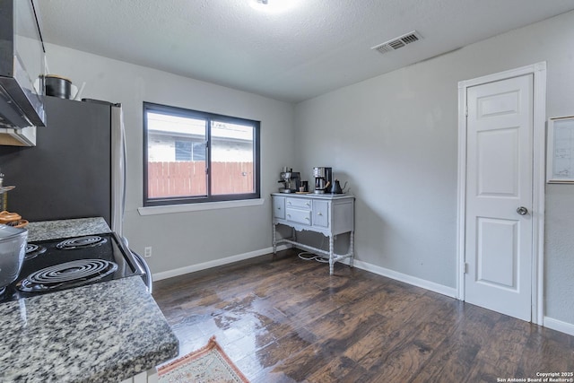 interior space with a textured ceiling, dark hardwood / wood-style floors, range with electric stovetop, stainless steel refrigerator, and light stone counters