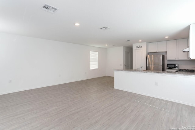 kitchen with light stone counters, white cabinets, stainless steel appliances, and light wood-type flooring