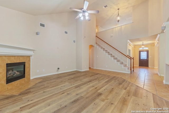 unfurnished living room featuring light hardwood / wood-style floors, high vaulted ceiling, a tiled fireplace, and ceiling fan with notable chandelier