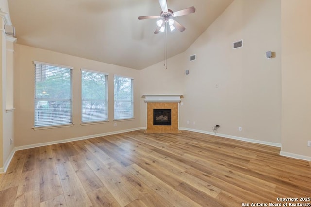 unfurnished living room with ceiling fan, a tile fireplace, high vaulted ceiling, and light hardwood / wood-style flooring