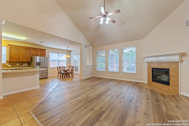 unfurnished living room featuring ceiling fan, light hardwood / wood-style floors, a fireplace, and high vaulted ceiling