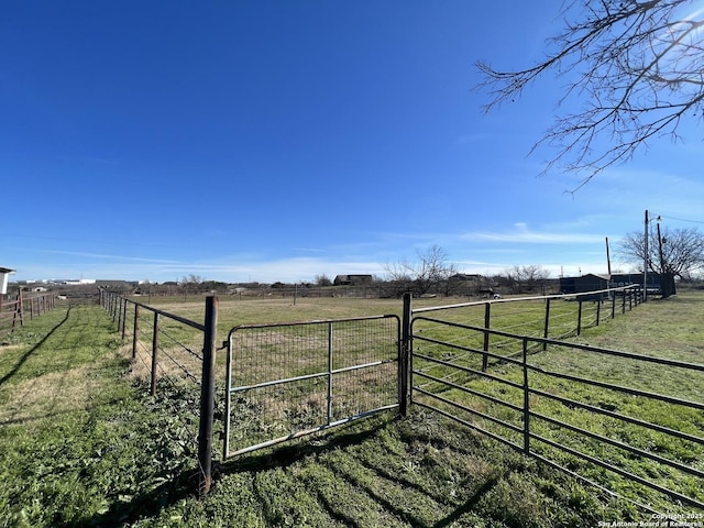 view of gate with a lawn and a rural view