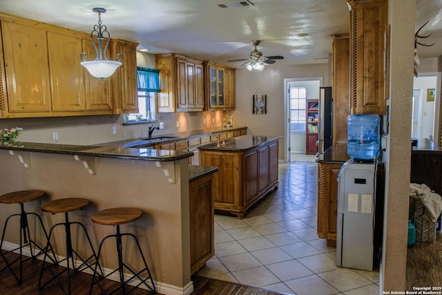 kitchen with pendant lighting, dark stone counters, ceiling fan, a breakfast bar, and light tile patterned floors