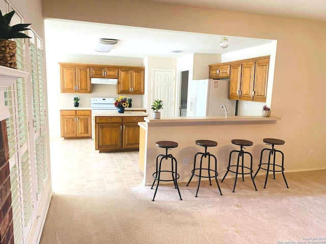 kitchen with a breakfast bar, light colored carpet, white refrigerator with ice dispenser, and kitchen peninsula