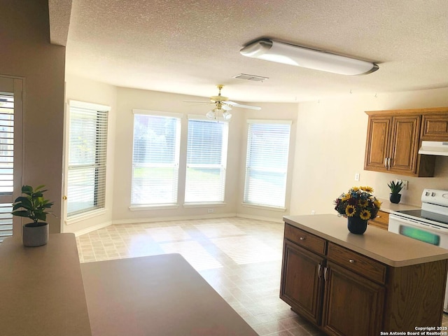 kitchen with a textured ceiling, ceiling fan, white electric range oven, and a center island