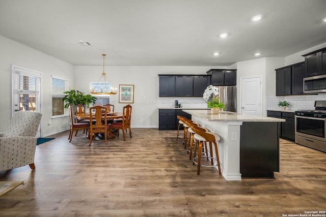 kitchen featuring tasteful backsplash, a center island, wood-type flooring, light stone countertops, and stainless steel appliances