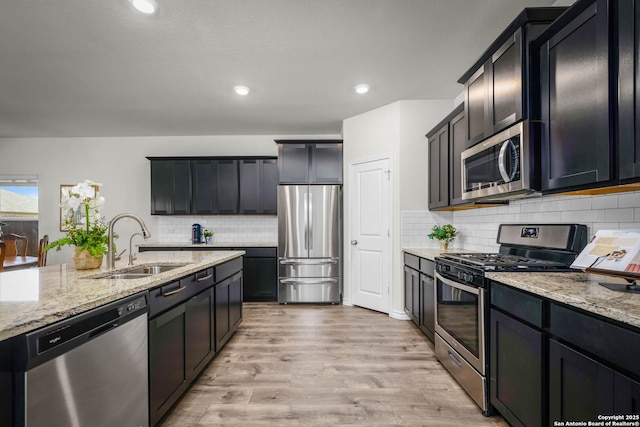 kitchen featuring appliances with stainless steel finishes, sink, light stone counters, and light hardwood / wood-style floors