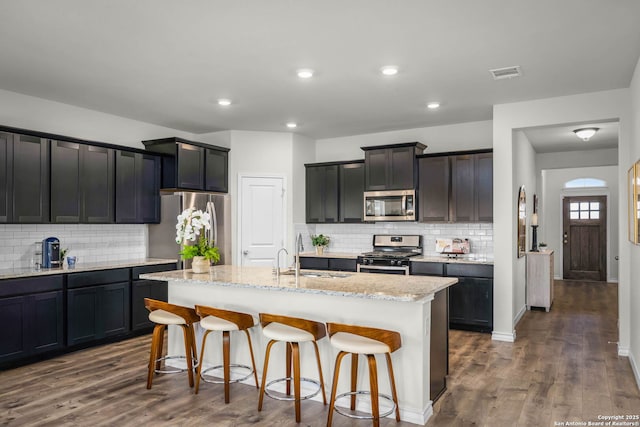 kitchen featuring a kitchen bar, an island with sink, stainless steel appliances, dark hardwood / wood-style floors, and sink