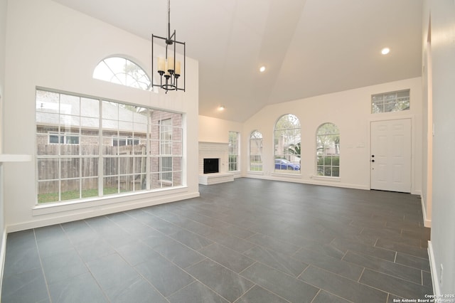 unfurnished living room featuring an inviting chandelier, a healthy amount of sunlight, and high vaulted ceiling