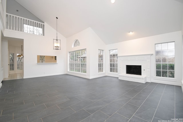 unfurnished living room with a brick fireplace, dark tile patterned flooring, an inviting chandelier, and high vaulted ceiling