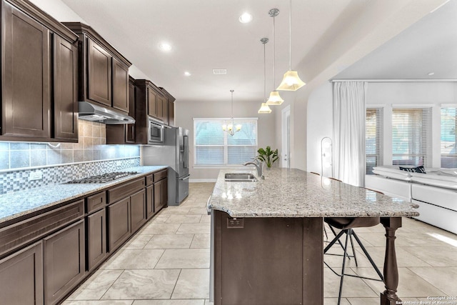 kitchen featuring tasteful backsplash, a notable chandelier, pendant lighting, sink, and a kitchen island with sink