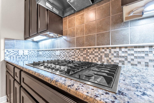 kitchen with light stone countertops, dark brown cabinetry, wall chimney exhaust hood, decorative backsplash, and stainless steel gas stovetop