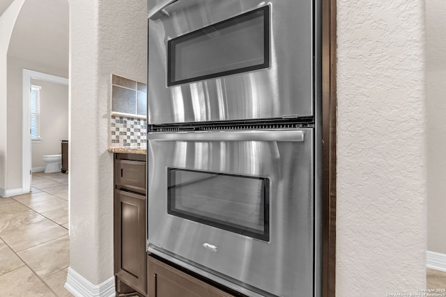 kitchen with light tile patterned floors, decorative backsplash, dark brown cabinets, and stainless steel double oven