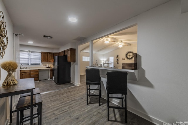 kitchen with a kitchen bar, hardwood / wood-style floors, kitchen peninsula, black fridge, and lofted ceiling with beams