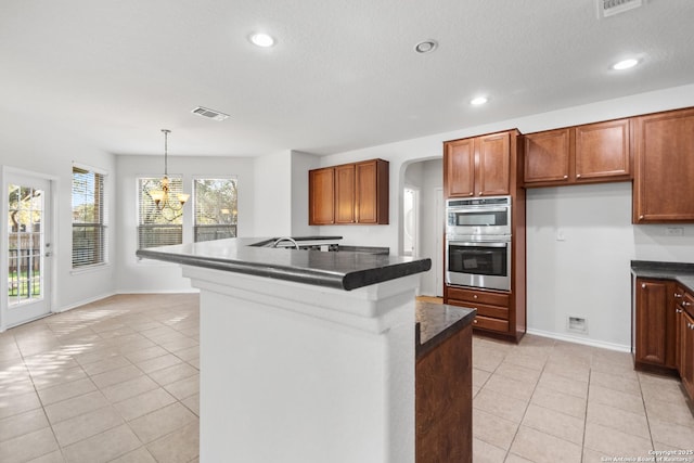 kitchen featuring pendant lighting, light tile patterned floors, a kitchen island with sink, stainless steel double oven, and a chandelier