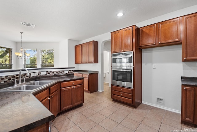 kitchen featuring tasteful backsplash, a chandelier, pendant lighting, double oven, and sink