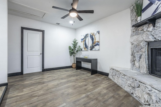 interior space featuring ceiling fan, dark hardwood / wood-style floors, and a stone fireplace