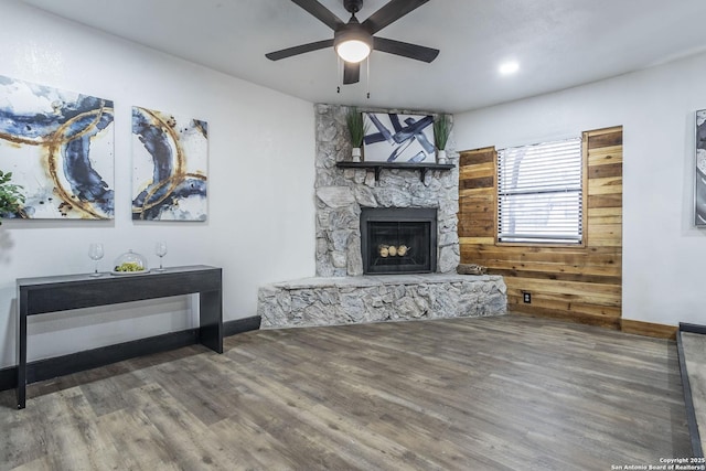 living room featuring ceiling fan, dark hardwood / wood-style flooring, and a stone fireplace