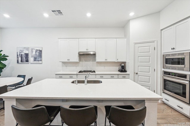 kitchen with white cabinets, decorative backsplash, stainless steel appliances, and a center island with sink