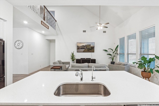 kitchen featuring ceiling fan, a center island with sink, sink, light stone countertops, and high vaulted ceiling