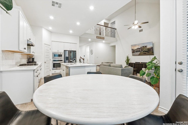 dining room with ceiling fan, light wood-type flooring, sink, and a high ceiling