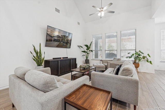 living room featuring light wood-type flooring, ceiling fan, and a high ceiling