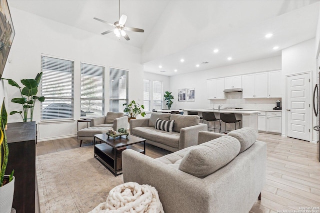 living room with high vaulted ceiling, ceiling fan, and light wood-type flooring