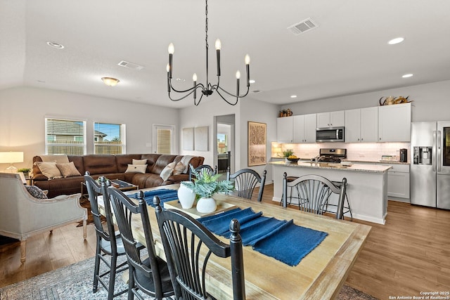 dining area with an inviting chandelier, lofted ceiling, and light hardwood / wood-style floors