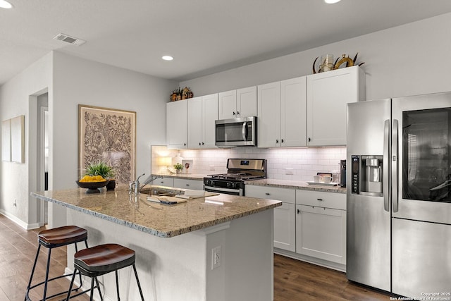 kitchen with an island with sink, stainless steel appliances, and white cabinetry