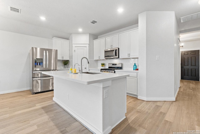 kitchen with appliances with stainless steel finishes, white cabinetry, an island with sink, decorative backsplash, and sink