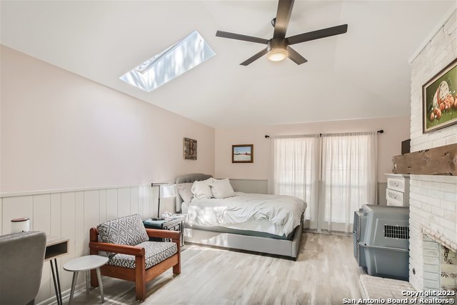 bedroom with ceiling fan, vaulted ceiling with skylight, light hardwood / wood-style flooring, and a fireplace