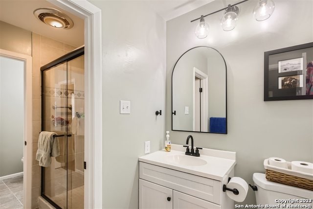 bathroom featuring toilet, vanity, tile patterned floors, and a shower with door