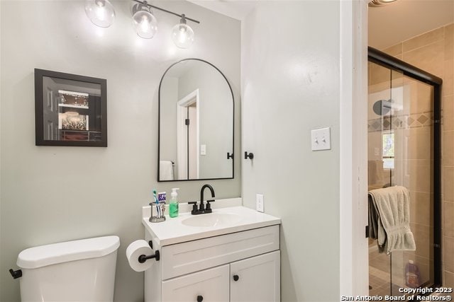 bathroom with toilet, vanity, and a shower with door