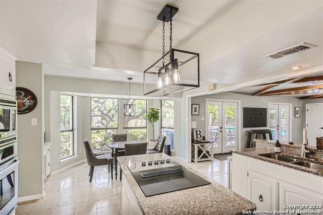 kitchen featuring pendant lighting, beamed ceiling, stainless steel oven, white cabinets, and french doors