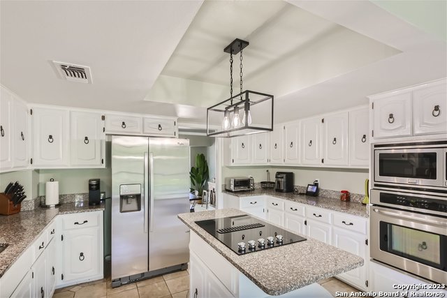 kitchen with appliances with stainless steel finishes, a center island, white cabinetry, hanging light fixtures, and light tile patterned floors