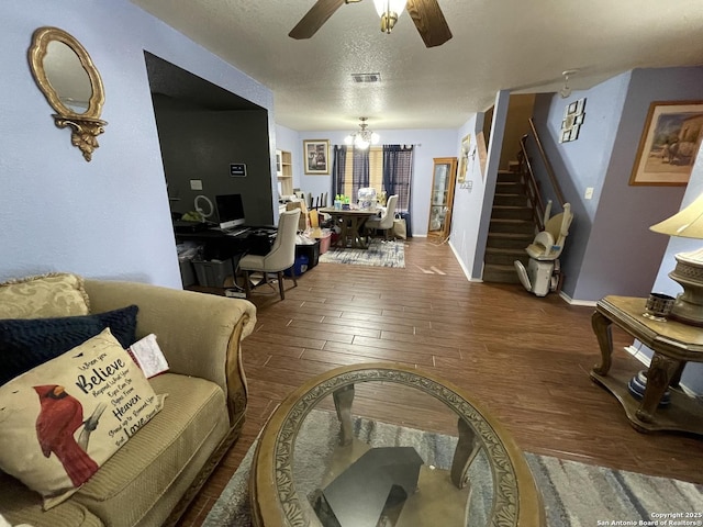 living room with dark wood-type flooring, ceiling fan with notable chandelier, and a textured ceiling