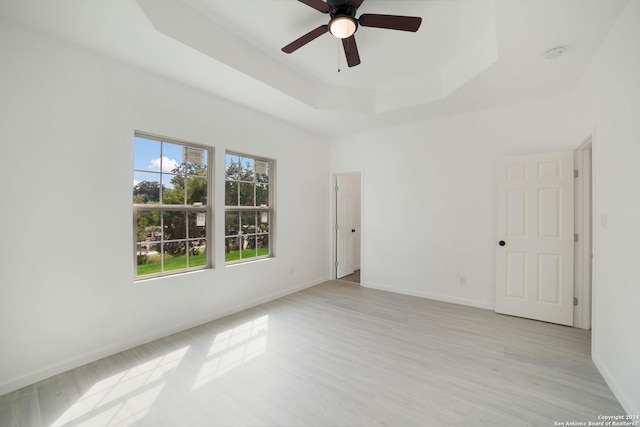 unfurnished room featuring ceiling fan, light hardwood / wood-style floors, and a tray ceiling