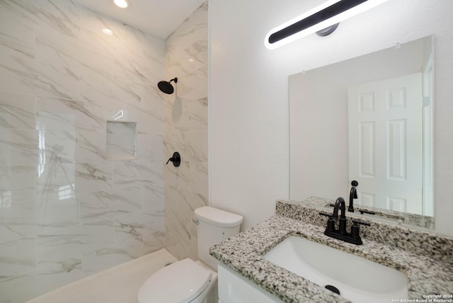 bathroom with toilet, tiled shower, and vanity