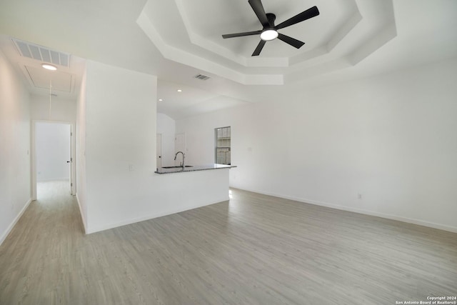 unfurnished living room featuring ceiling fan, a tray ceiling, and light hardwood / wood-style flooring