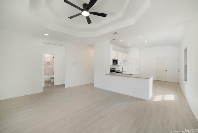 unfurnished living room featuring ceiling fan, light hardwood / wood-style floors, a tray ceiling, and sink