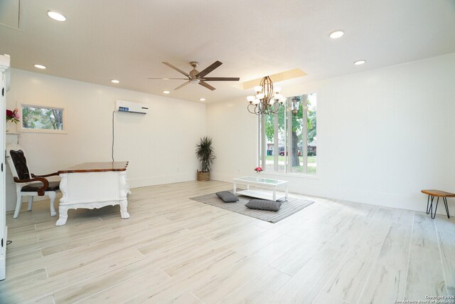 interior space featuring a wall mounted AC, light wood-type flooring, and ceiling fan with notable chandelier