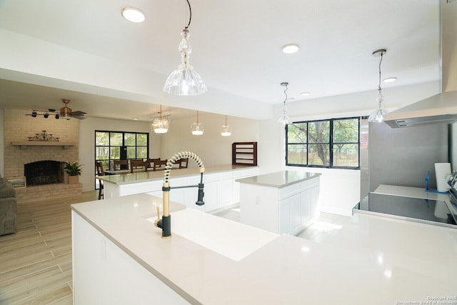 kitchen featuring pendant lighting, white cabinets, a fireplace, ventilation hood, and a center island with sink