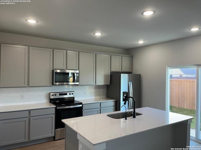 kitchen featuring tasteful backsplash, gray cabinets, sink, appliances with stainless steel finishes, and an island with sink