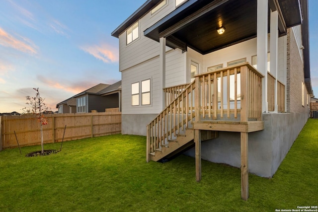 back house at dusk featuring a deck and a lawn