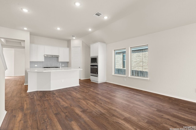 kitchen with appliances with stainless steel finishes, dark hardwood / wood-style floors, an island with sink, decorative backsplash, and white cabinets