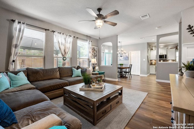 living room featuring ceiling fan with notable chandelier, hardwood / wood-style floors, and a textured ceiling