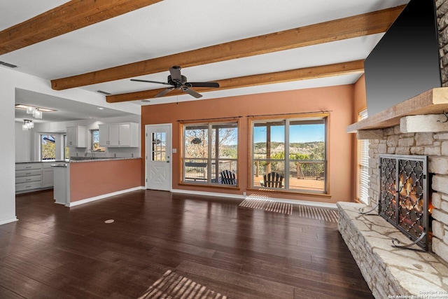 unfurnished living room with ceiling fan, dark hardwood / wood-style flooring, beamed ceiling, and a stone fireplace