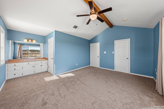 unfurnished bedroom with ceiling fan, light colored carpet, connected bathroom, and vaulted ceiling with beams