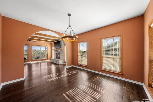 unfurnished living room with beamed ceiling, a stone fireplace, a chandelier, and hardwood / wood-style flooring