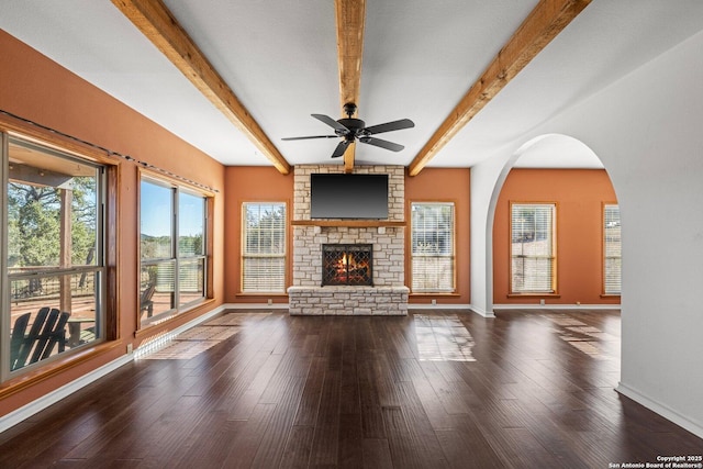 unfurnished living room featuring beam ceiling, ceiling fan, dark hardwood / wood-style floors, and a stone fireplace